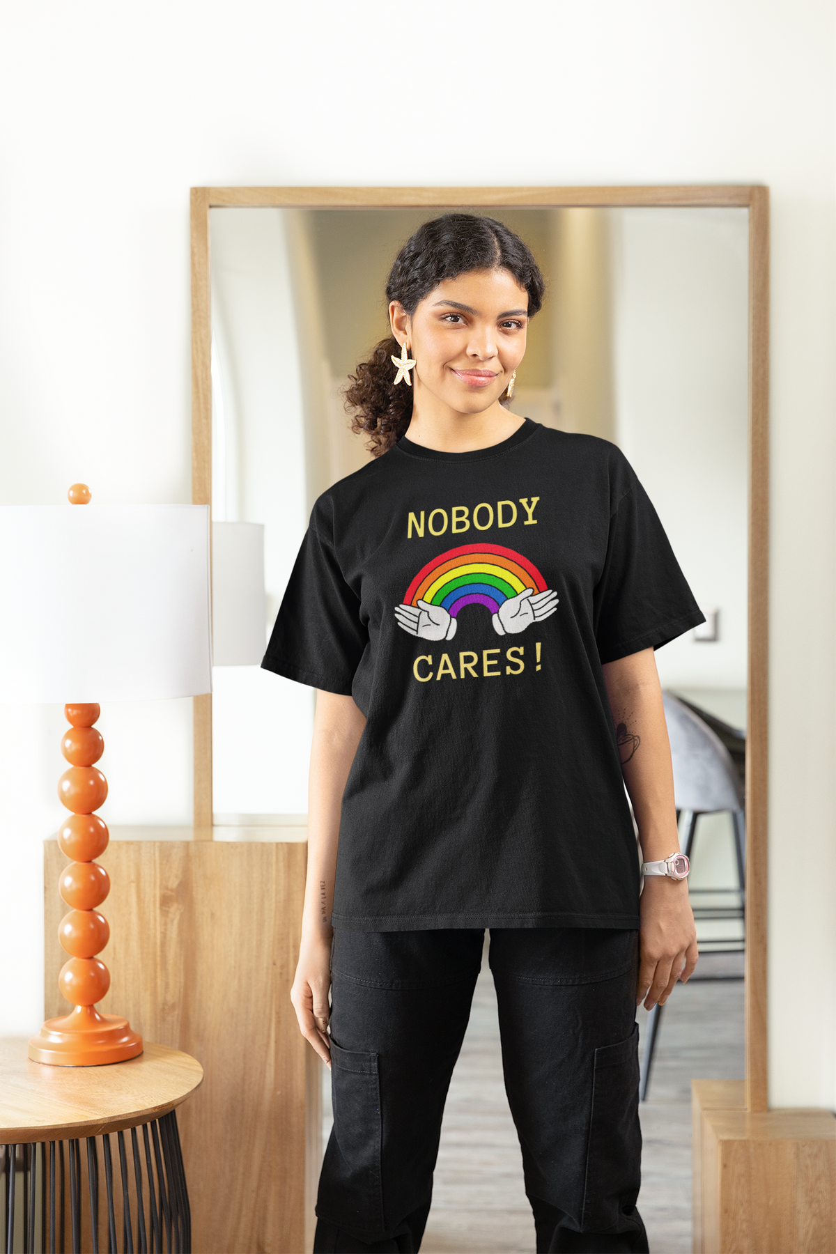 "Nobody Cares" rainbow women's tee in black, woman modeling it at home, funny sarcastic gift shirt