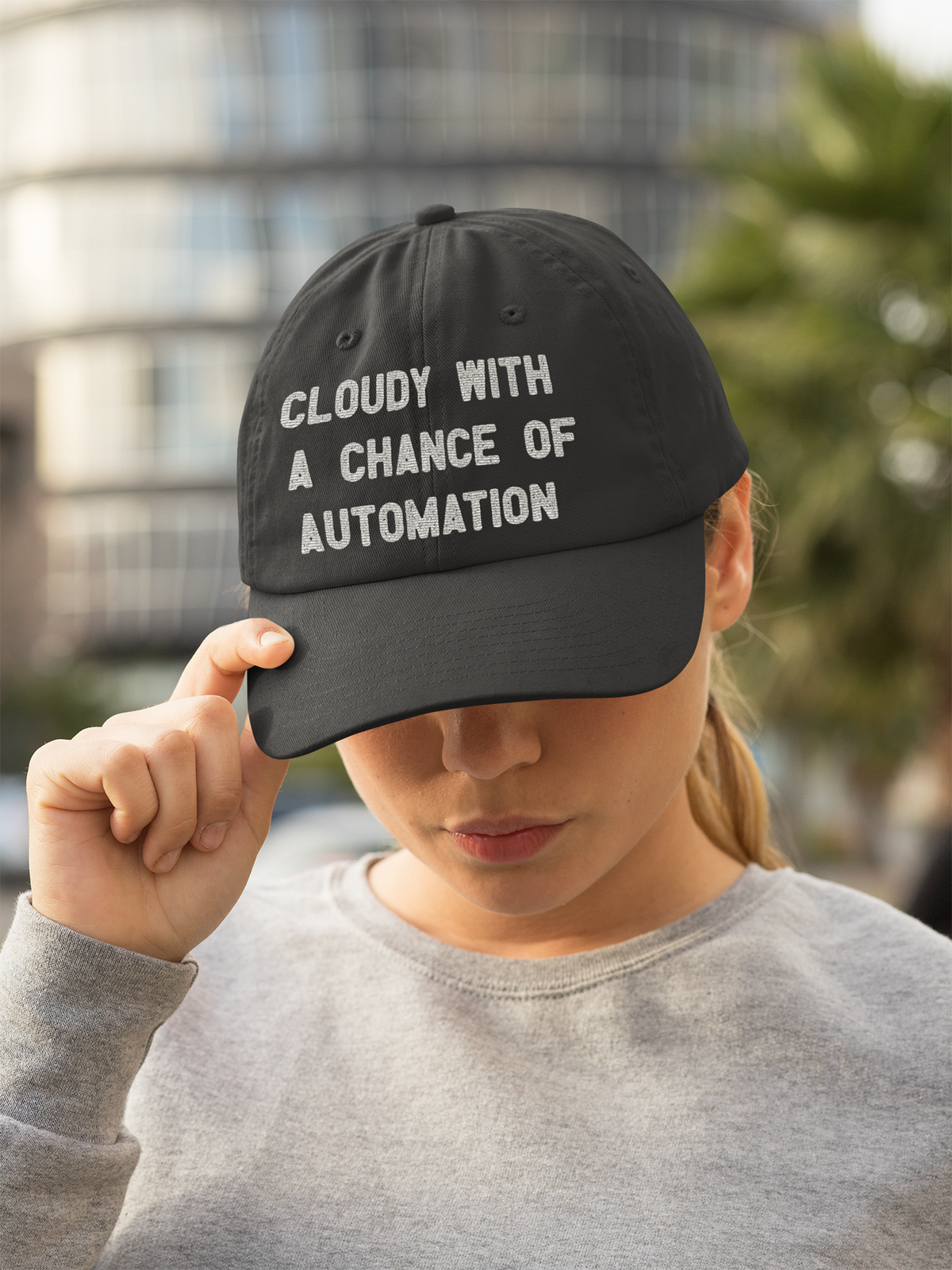 'Cloudy With a Chance of Automation' dad hat in black, woman wearing it outdoors, funny gift for cloud engineers