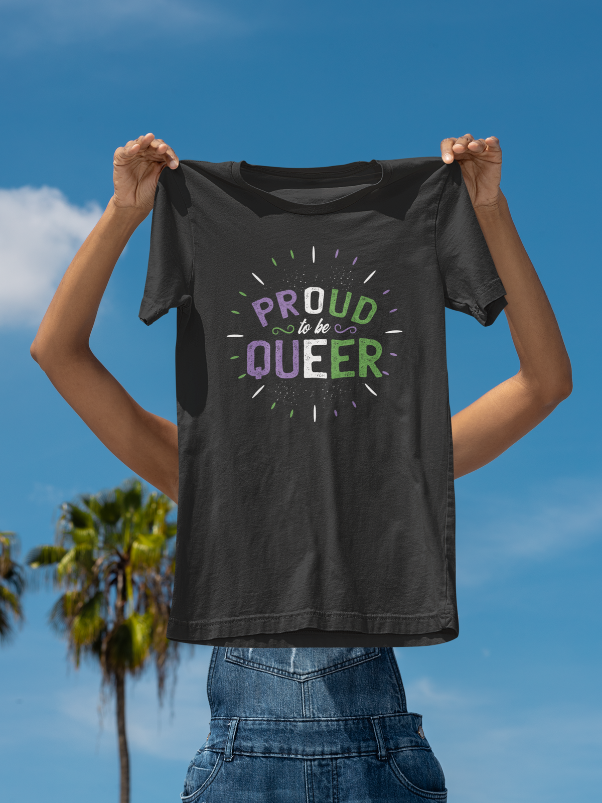 'Proud to Be Queer' T-shirt in black, held up outdoors against a blue sky, funny pride gift shirt