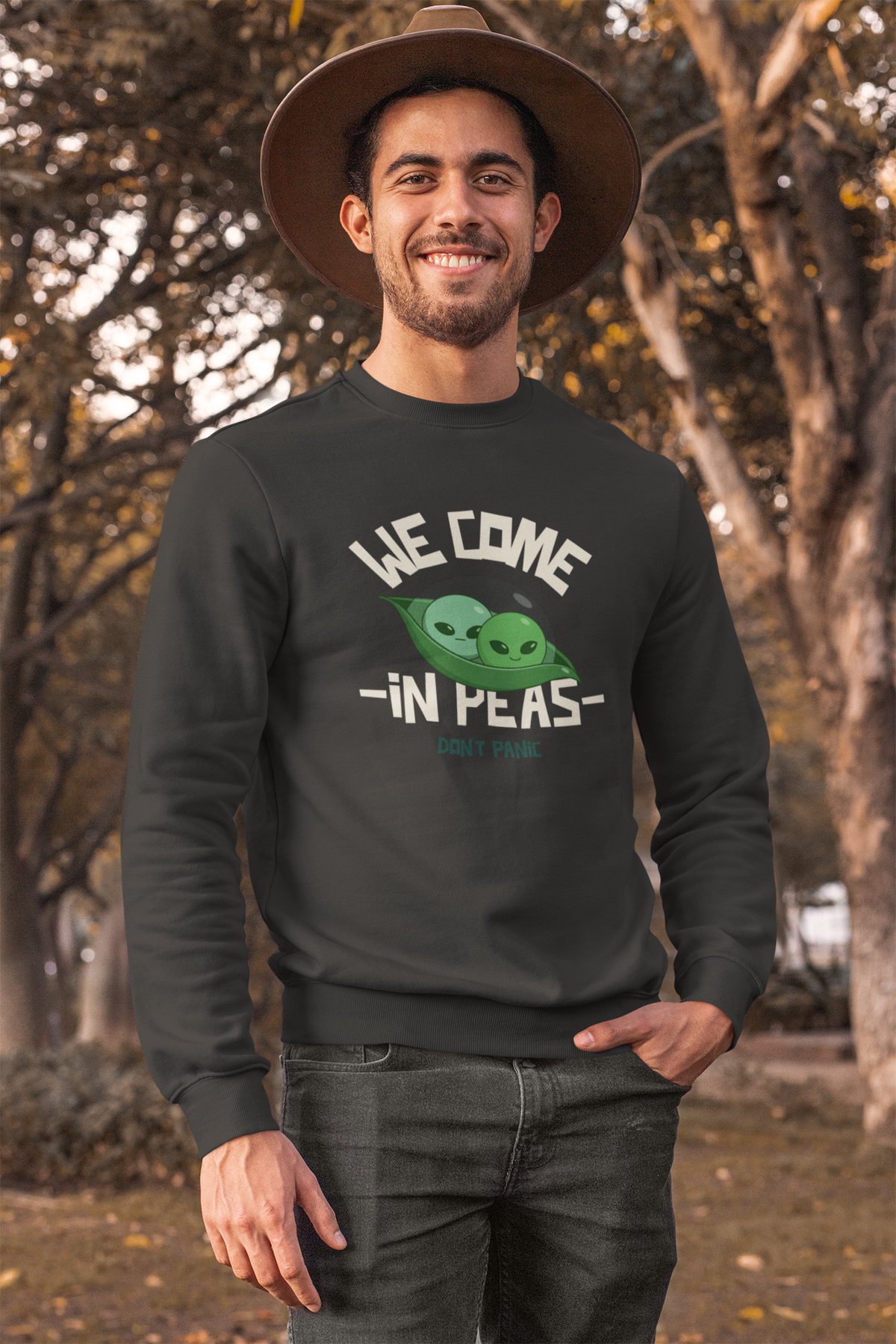 'We Come in Peas' pea pun sweatshirt in graphite heather, man wearing it outdoors in a park, funny alien crewneck gift idea