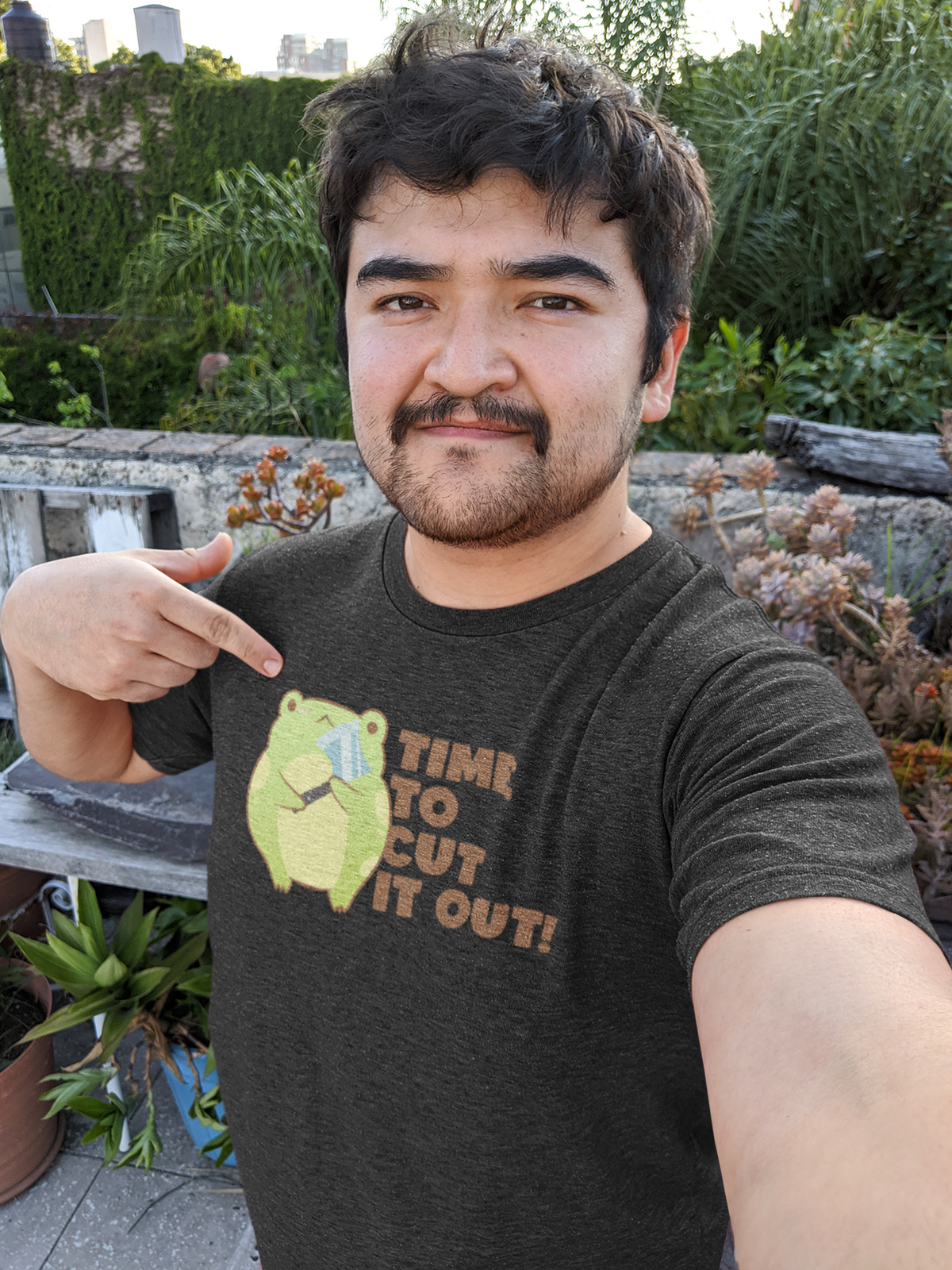 'Time to Cut It Out' frog t-shirt in black, man wearing it in garden, funny science pun shirt gift