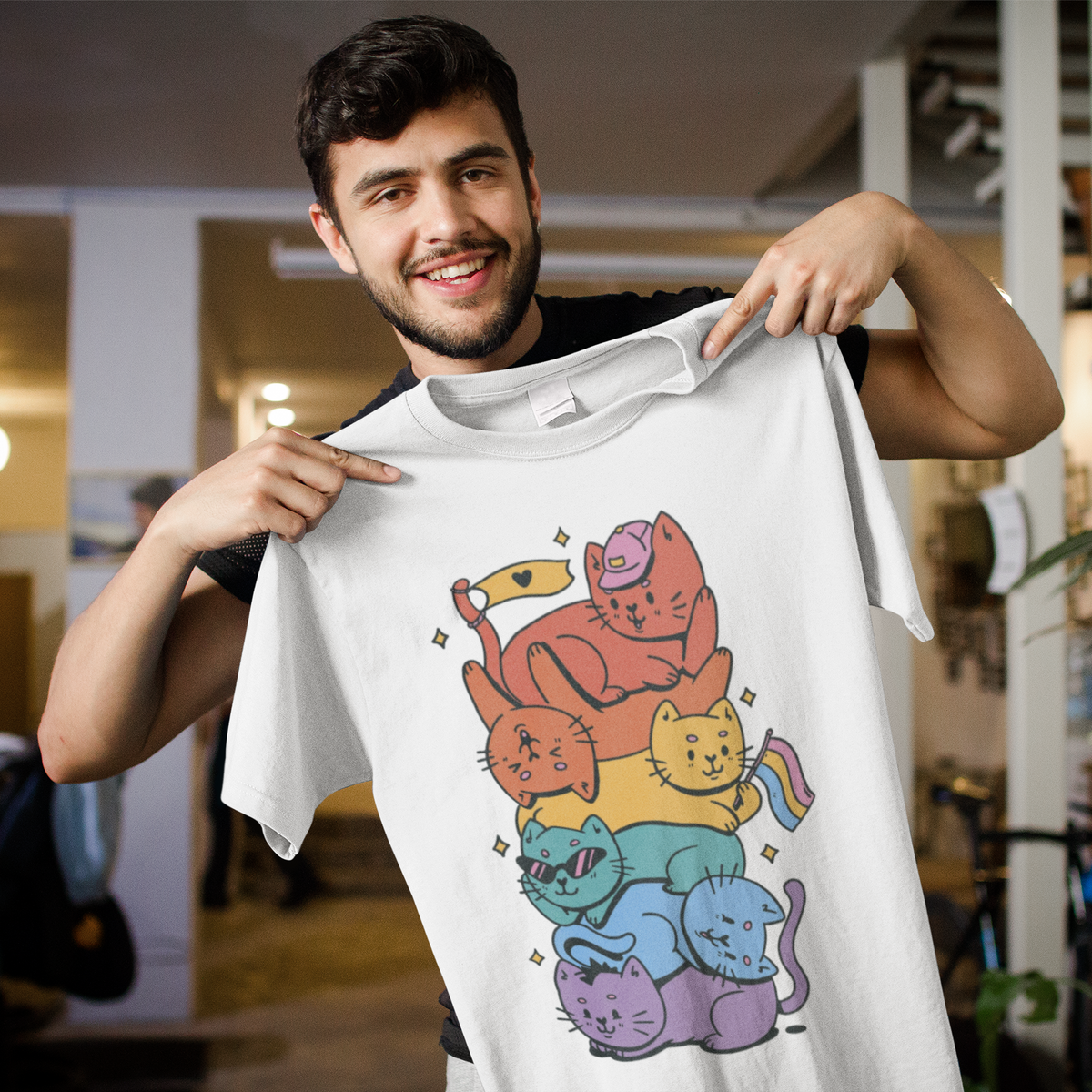 'Pride Stack of Cats' t-shirt in white, man model holding it up on a hanger indoors