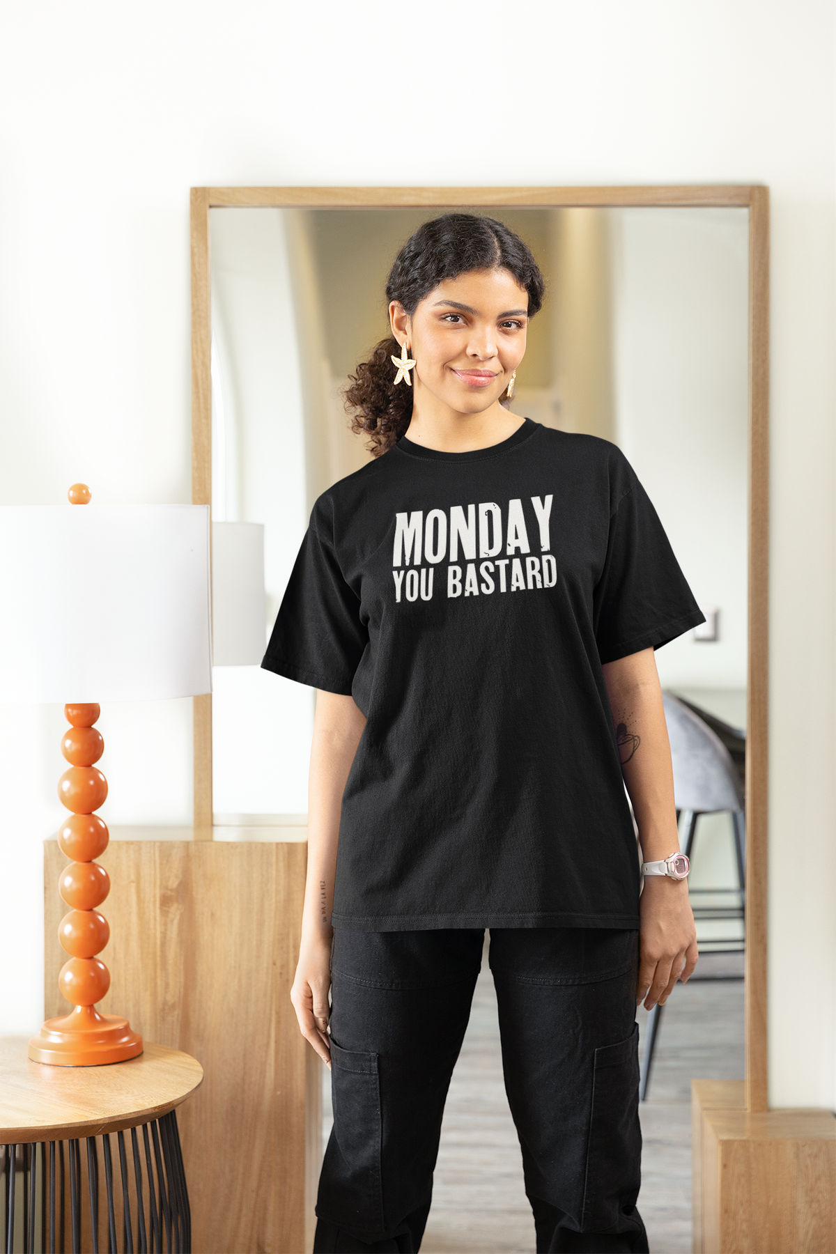 'Monday You Bastard' women's t-shirt in black, woman standing indoors by a mirror, funny sarcastic gift