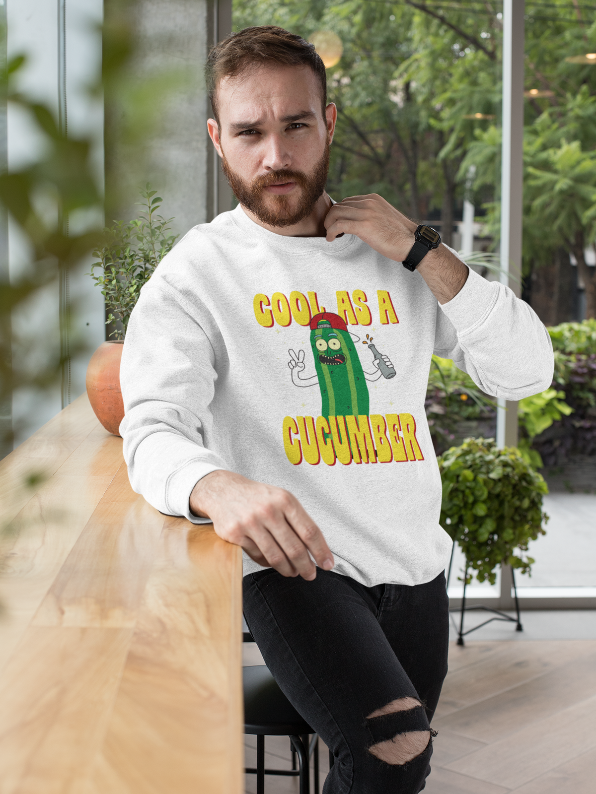 "Cool As A Cucumber" cartoon graphic sweatshirt in white, bearded man wearing it seated indoors, funny gift