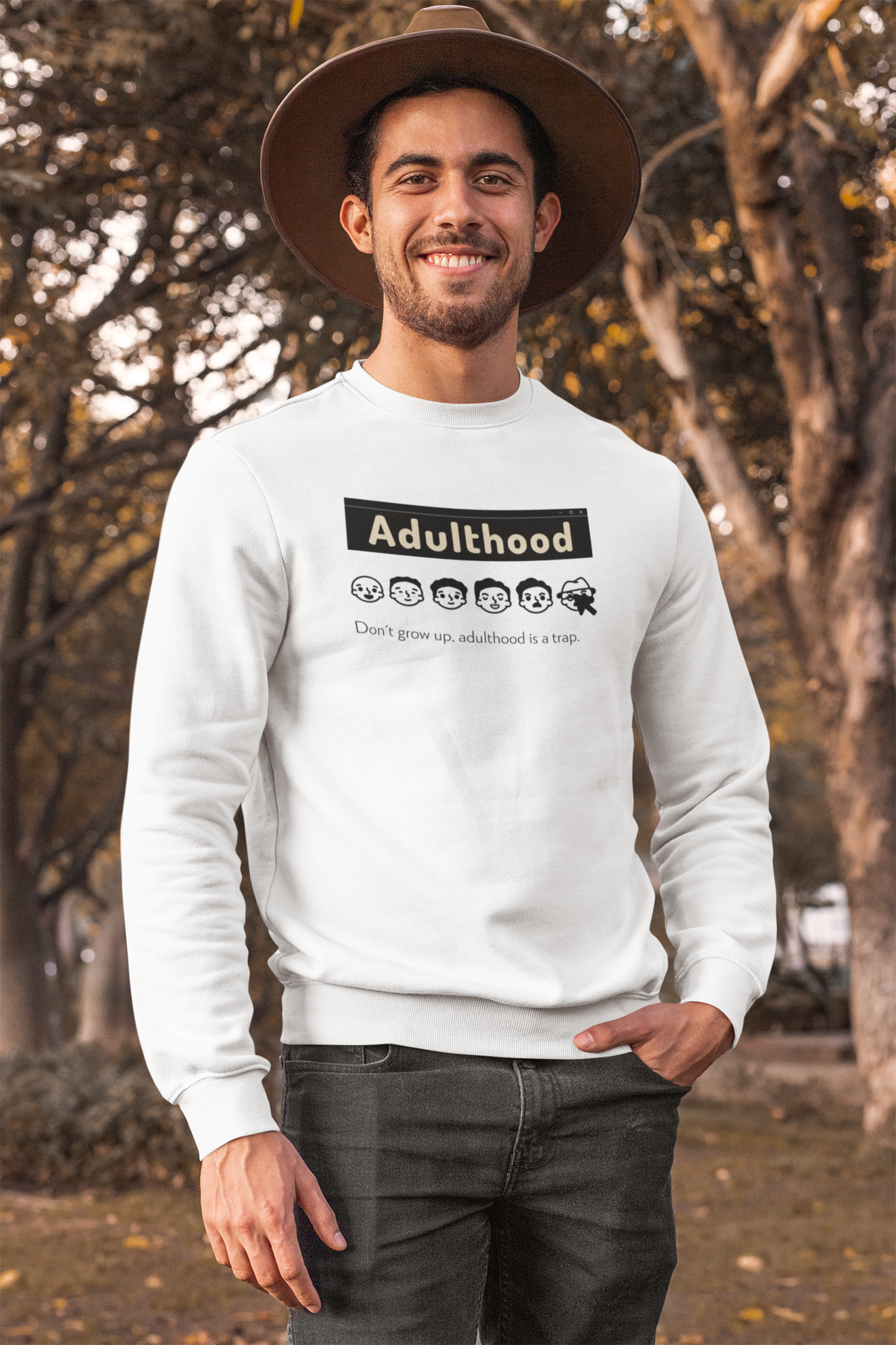 'Adulthood is a Trap' sweatshirt in white, man wearing it in a park, funny sarcastic gift idea