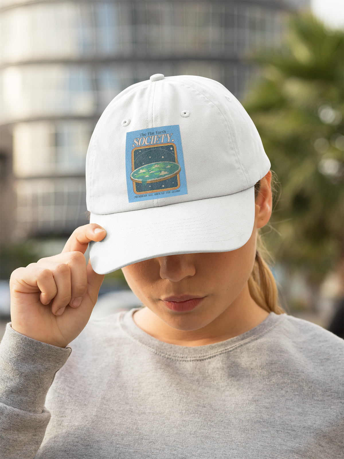 'The Flat Earth Society' dad hat in white, woman wearing it outdoors, funny satire hat gift idea