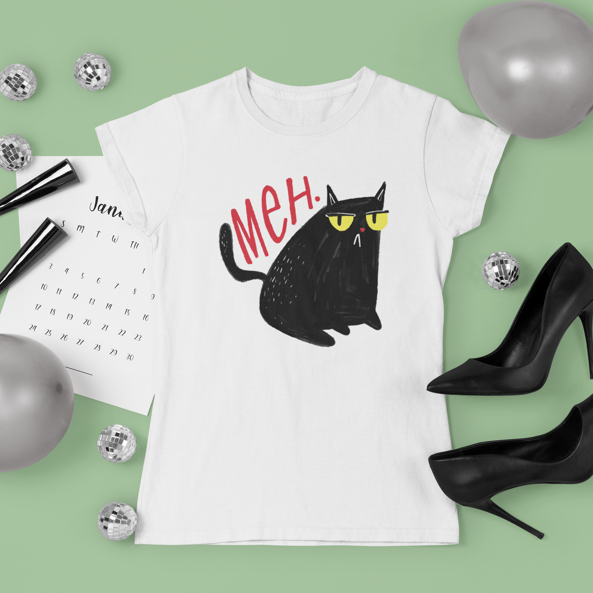 'Meh' black cat T-shirt in white, flat lay on a green backdrop, funny gift for cat lovers