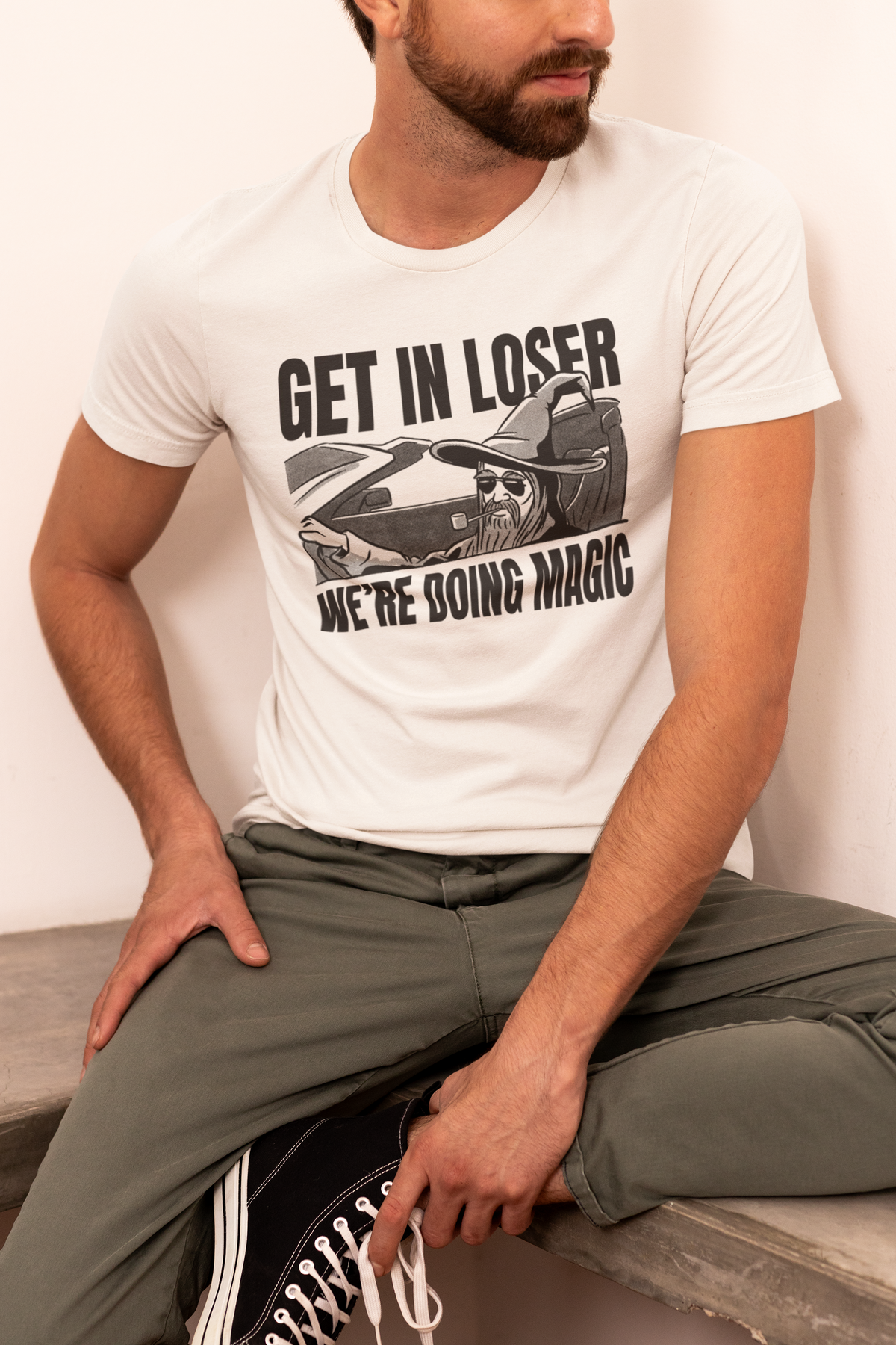 'Get In Loser, We're Doing Magic' t-shirt in white, man model seated wearing it, funny gift for dungeon masters