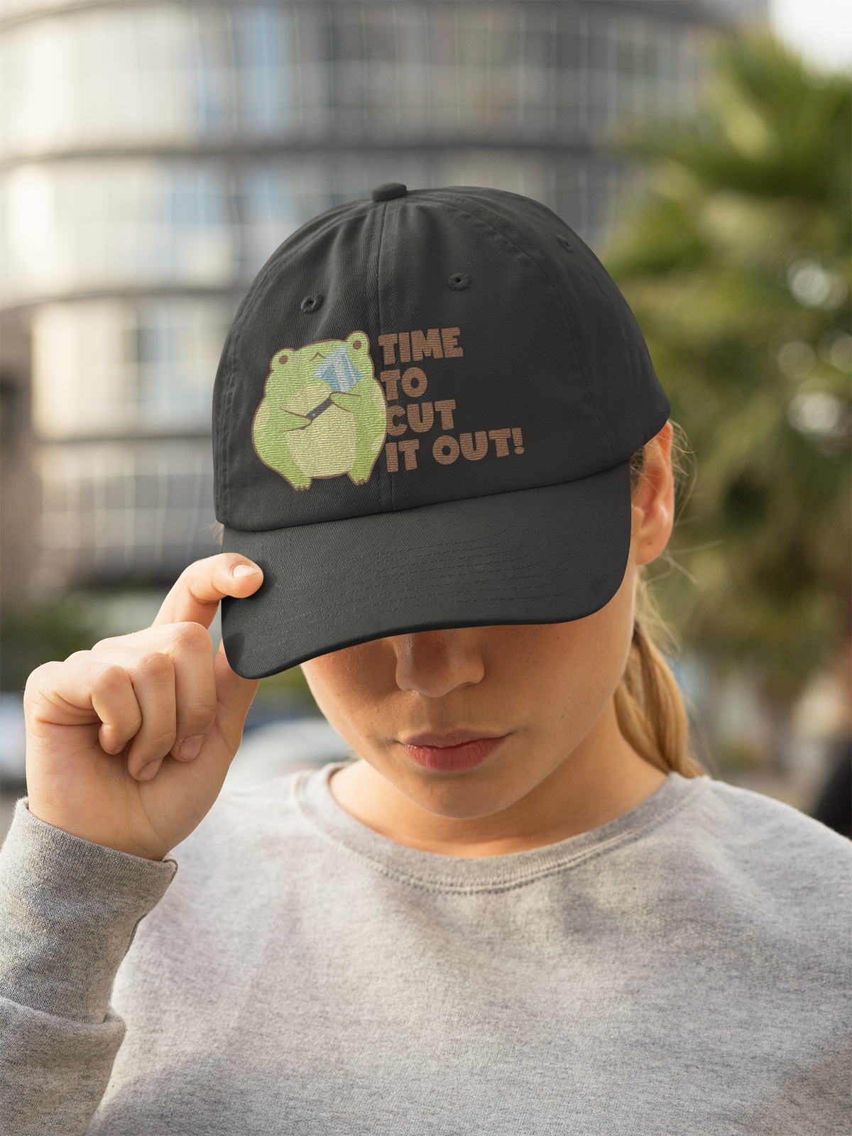 'Time to Cut It Out' frog dad hat in black, woman wearing it outdoors, funny science pun hat gift