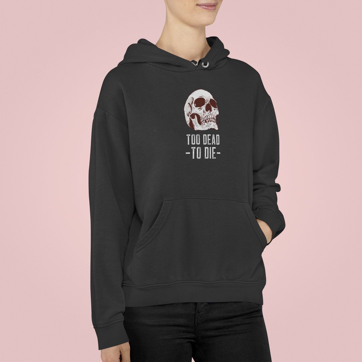 'Too Dead To Die' skull graphic hoodie in black, woman wearing it against a pink backdrop, gothic gift