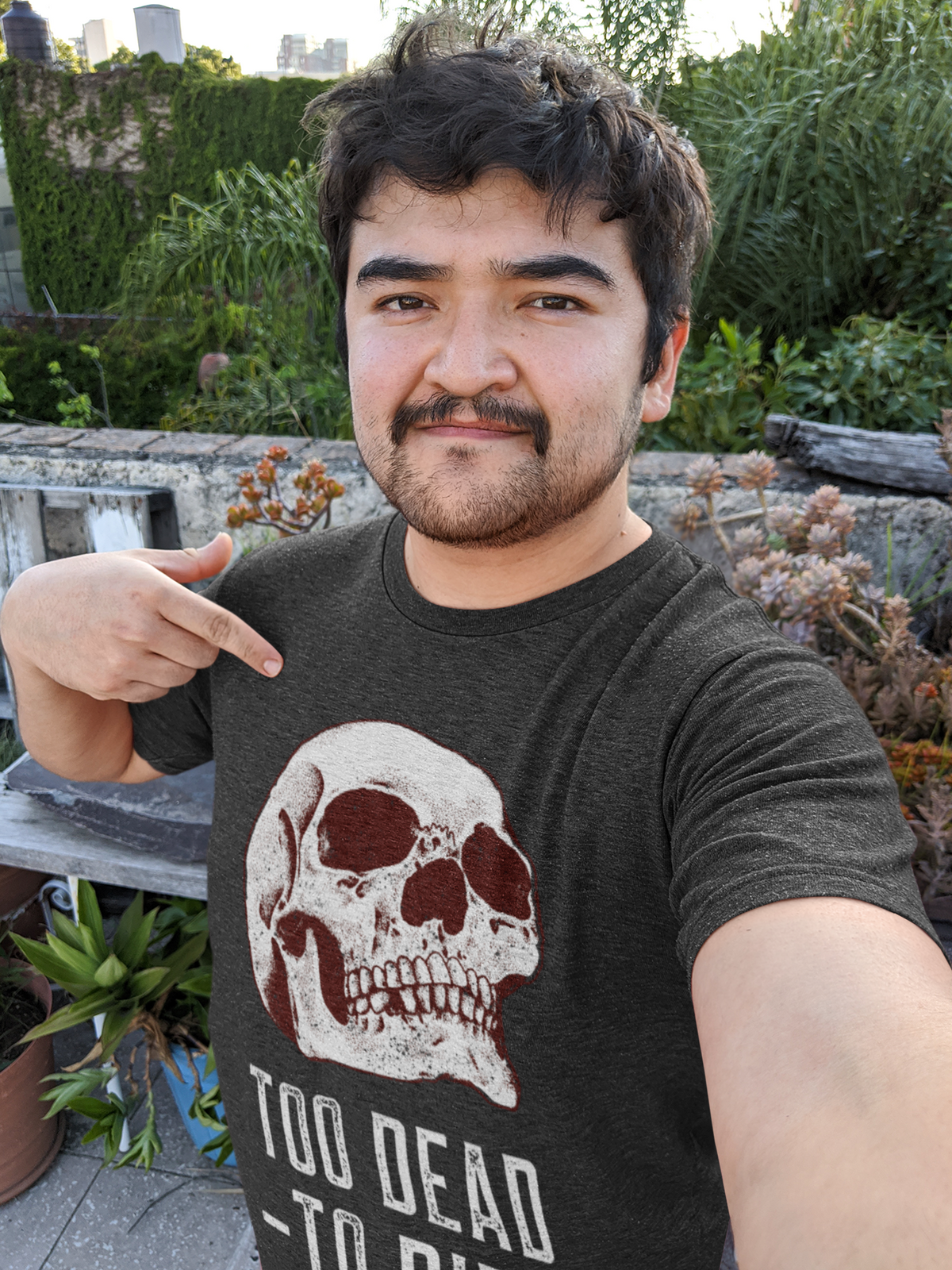 'Too Dead To Die' skull t-shirt in black, man wearing it outdoors in a garden, funny gift for goths