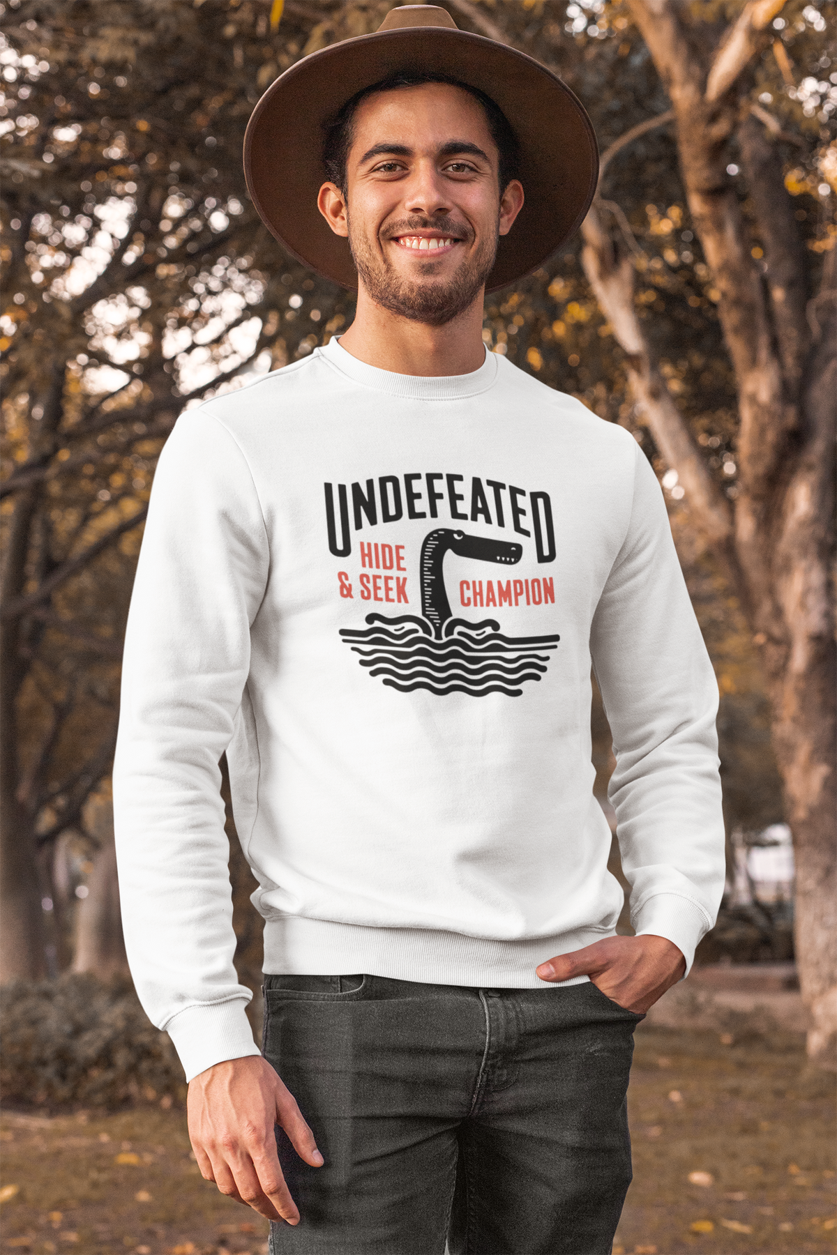 "Undefeated Hide and Seek Champion" sweatshirt in white, man wearing it outdoors, funny game gift