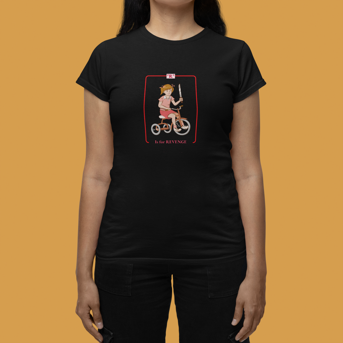 'R is for Revenge' tricycle girl graphic women's tee in black, woman wearing it on orange backdrop, funny gift