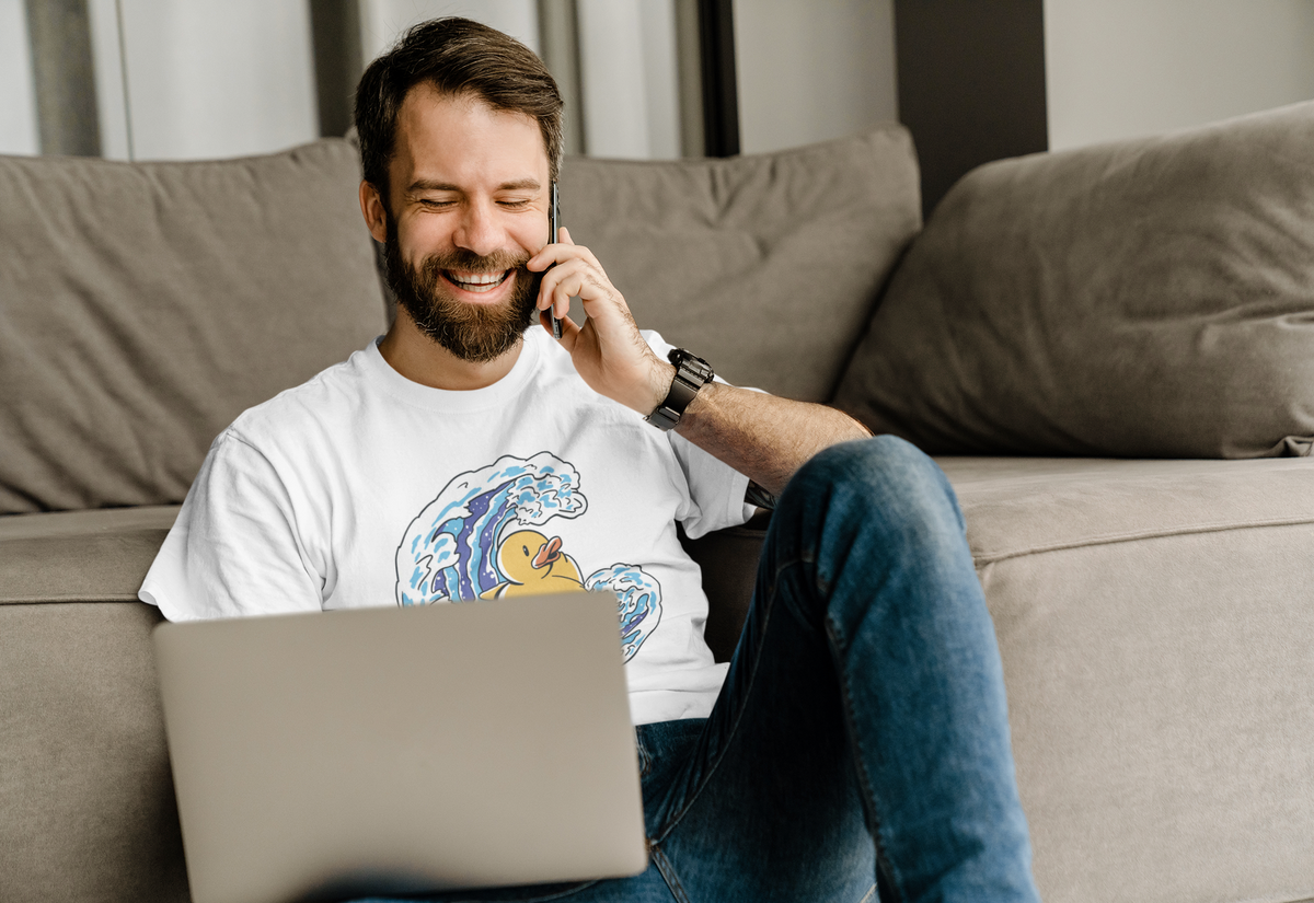 Surfing duck t-shirt in white, man model wearing it on a couch with a laptop, funny gift for surfers