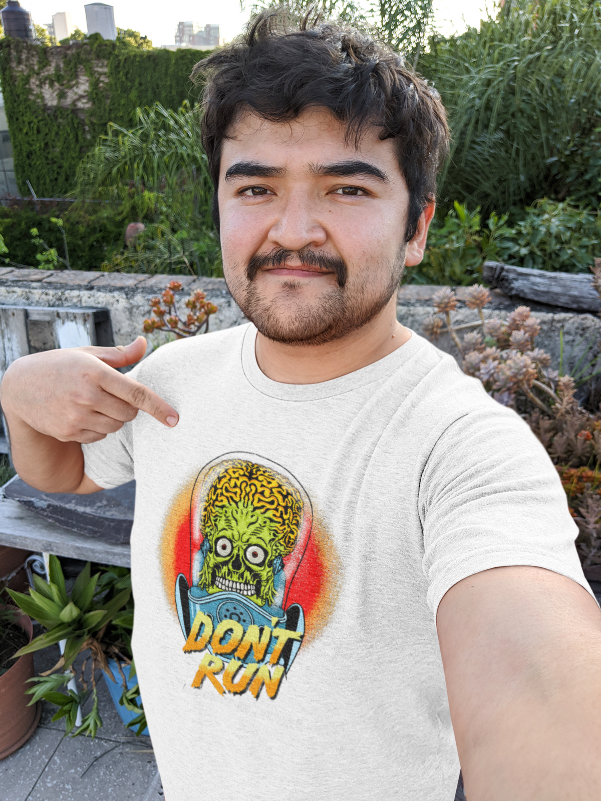 "Don't Run We Come In Peace" alien graphic t-shirt in white, man wearing it outdoors, quirky sci-fi lover gift