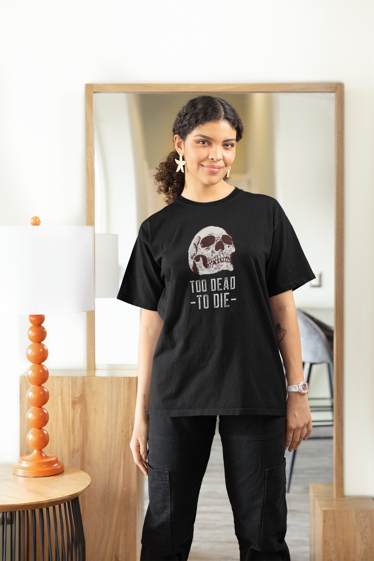 'Too Dead To Die' skull graphic women's t-shirt in black, woman standing indoors by a mirror, gothic gift