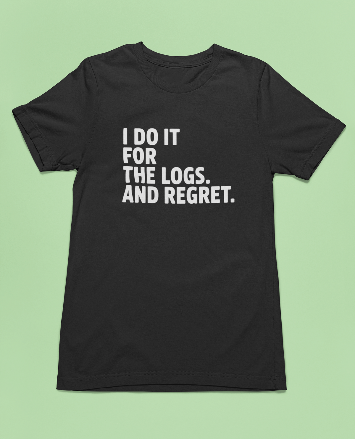 'I Do It For The Logs. And Regret.' t-shirt in black, flat lay on pale green background, funny developer gift