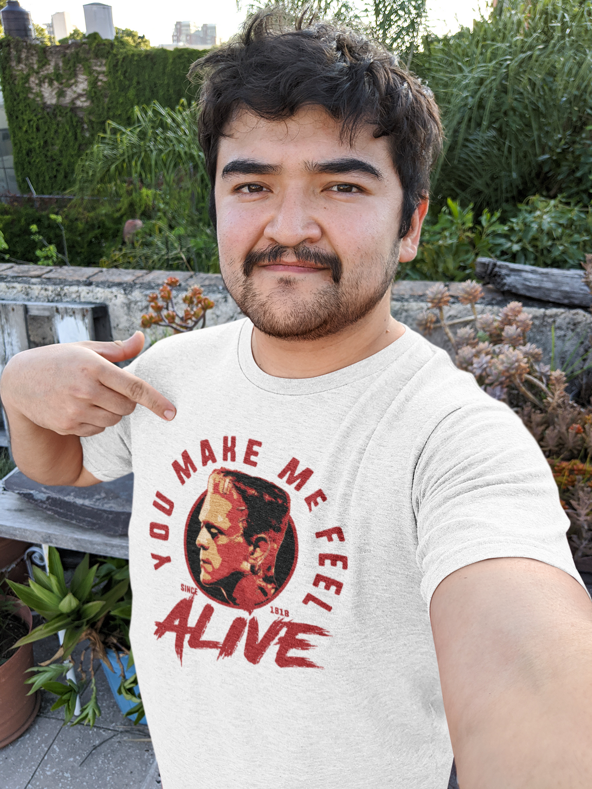 'You Make Me Feel Alive' t-shirt in heather white, man pointing at print outdoors, music fan tee