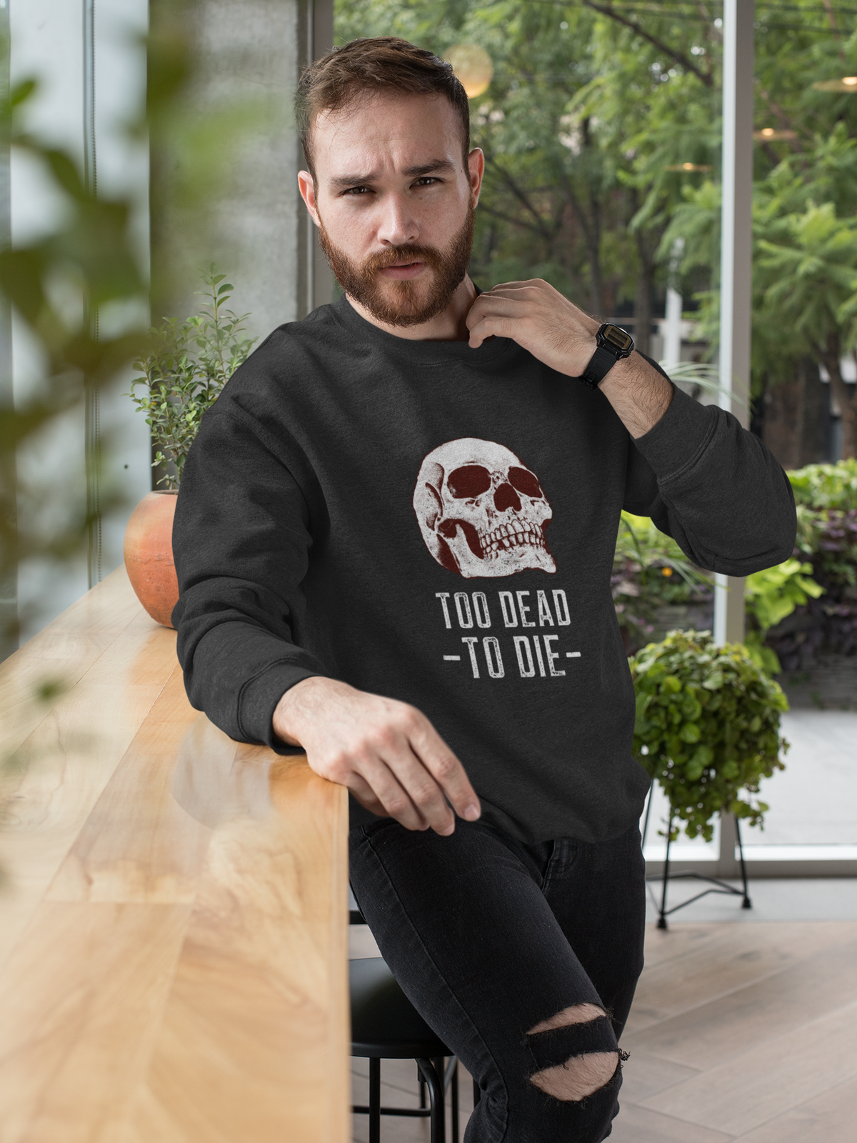 'Too Dead To Die' skull graphic sweatshirt in black, bearded man sitting indoors, funny gothic gift