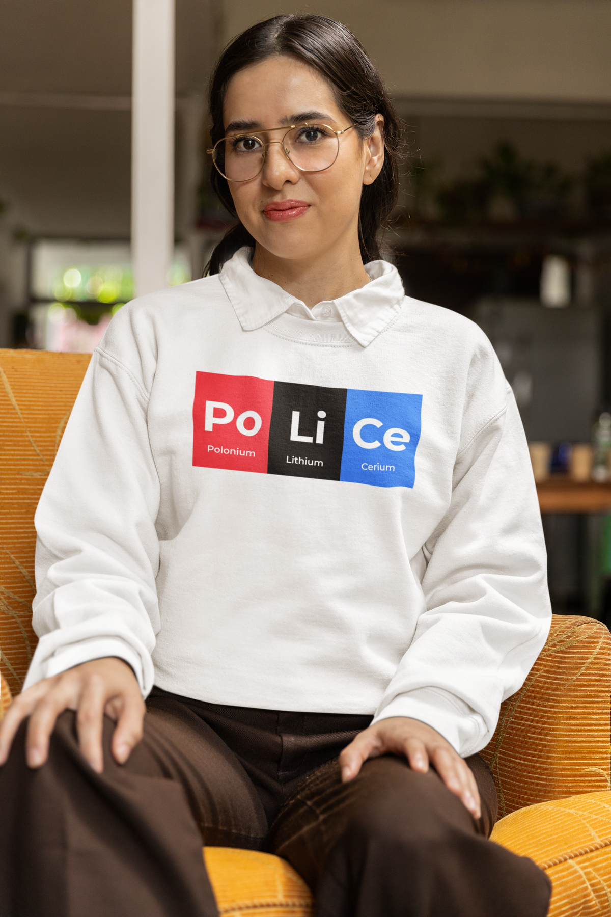 'Po-Li-Ce' periodic table sweatshirt in heather grey, woman sitting in an armchair wearing it, cozy photo