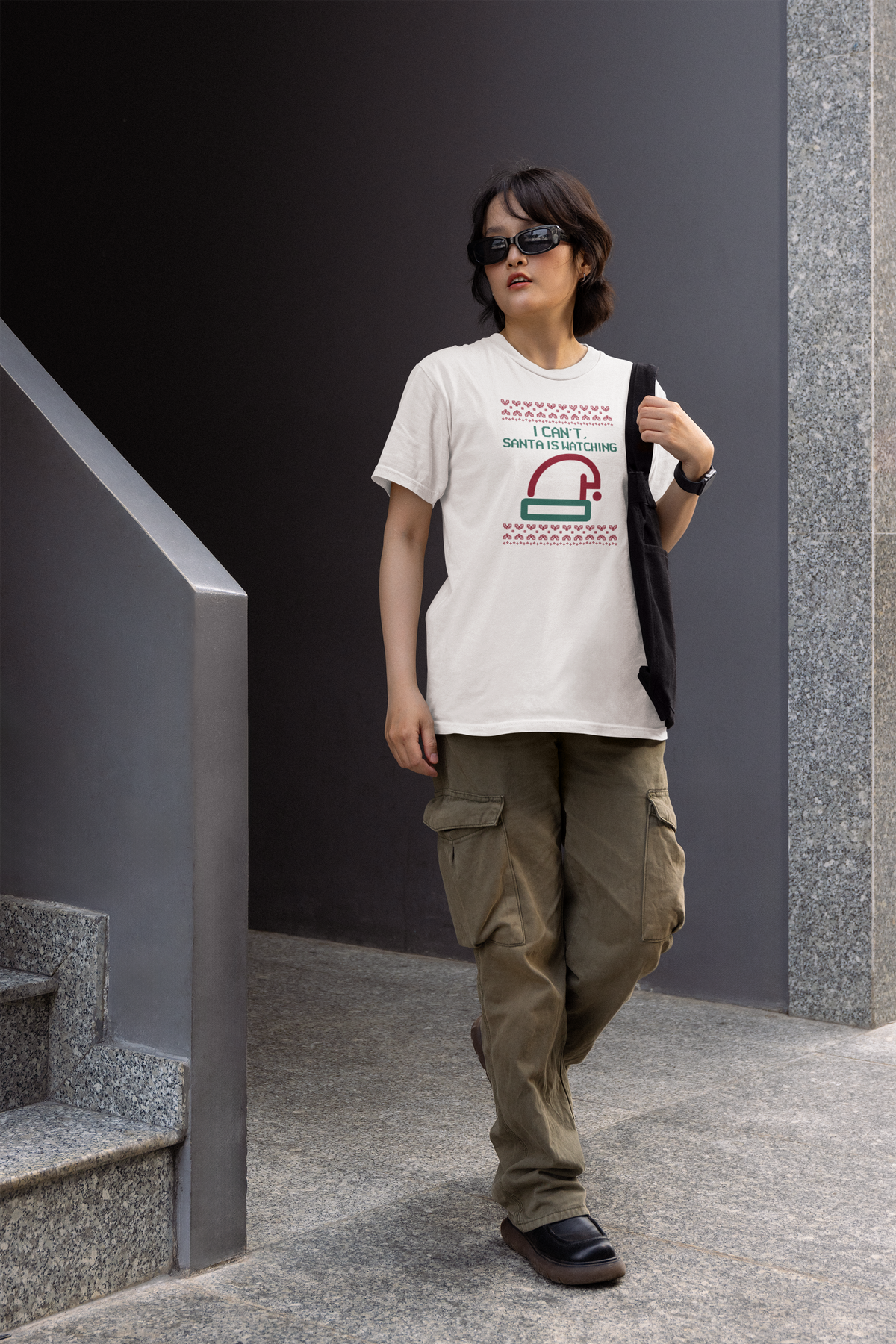 'I Can't Santa Is Watching' camera graphic tee in white, woman walking in urban setting, funny Christmas gift