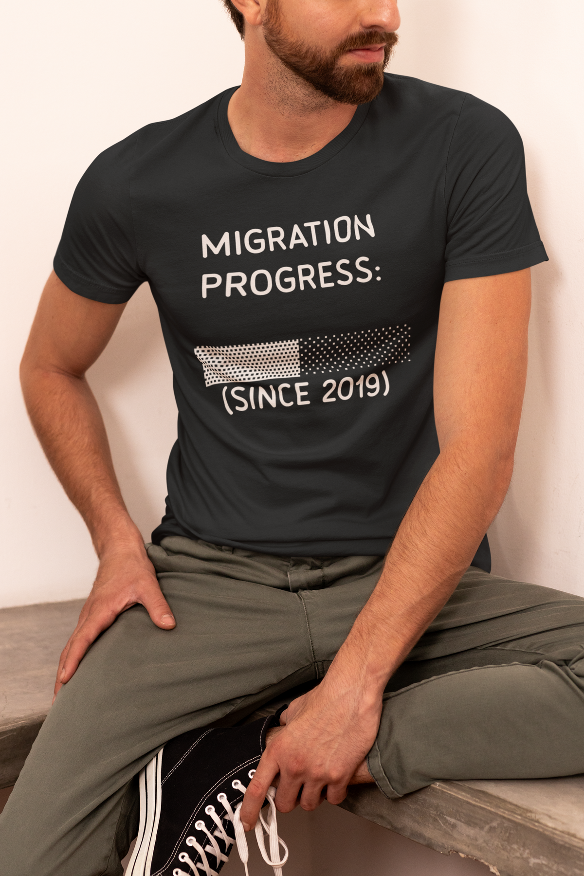 'Migration Progress: (Since 2019)' t-shirt in black, man sitting outdoors, funny sysadmin gift for coders