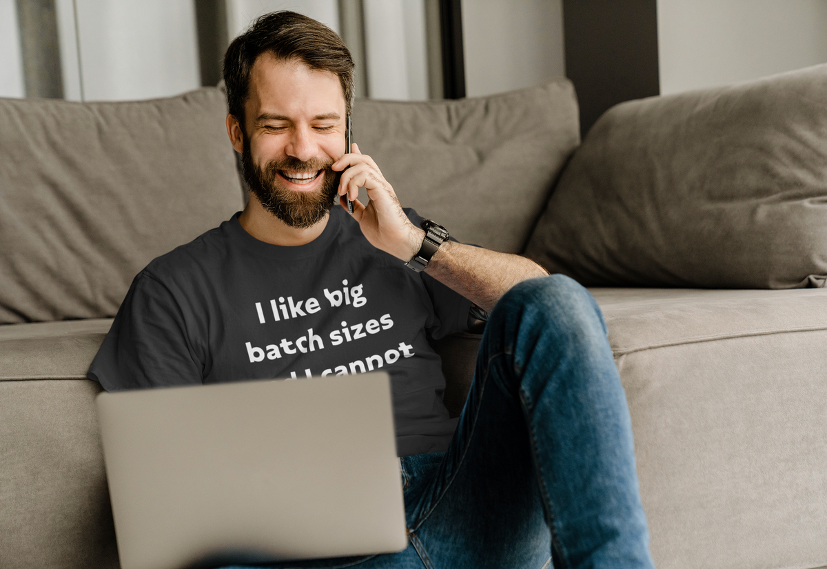 'I Like Big Batch Sizes and I Cannot Lie' t-shirt in black, man wearing it on couch on phone, funny developer gift