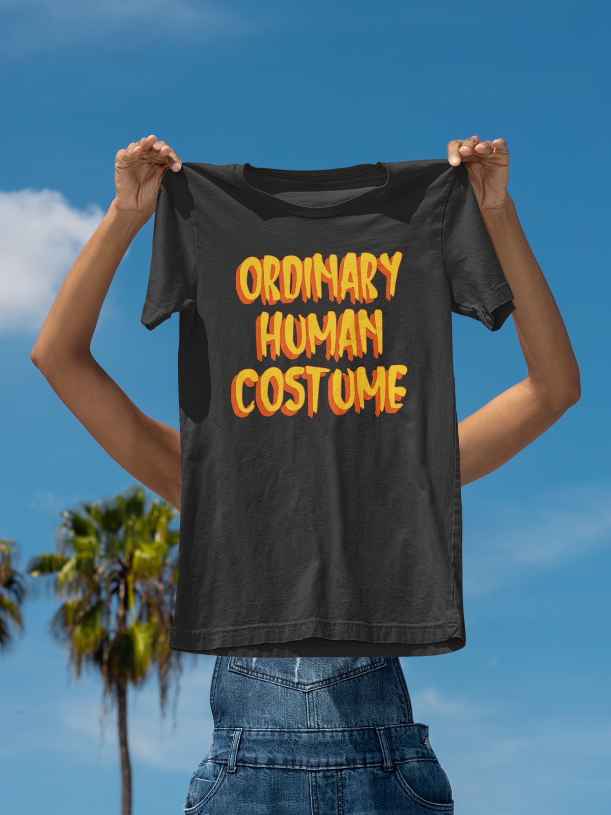 'Ordinary Human Costume' funny halloween t-shirt in black, man holding it up outdoors, funny costume gift