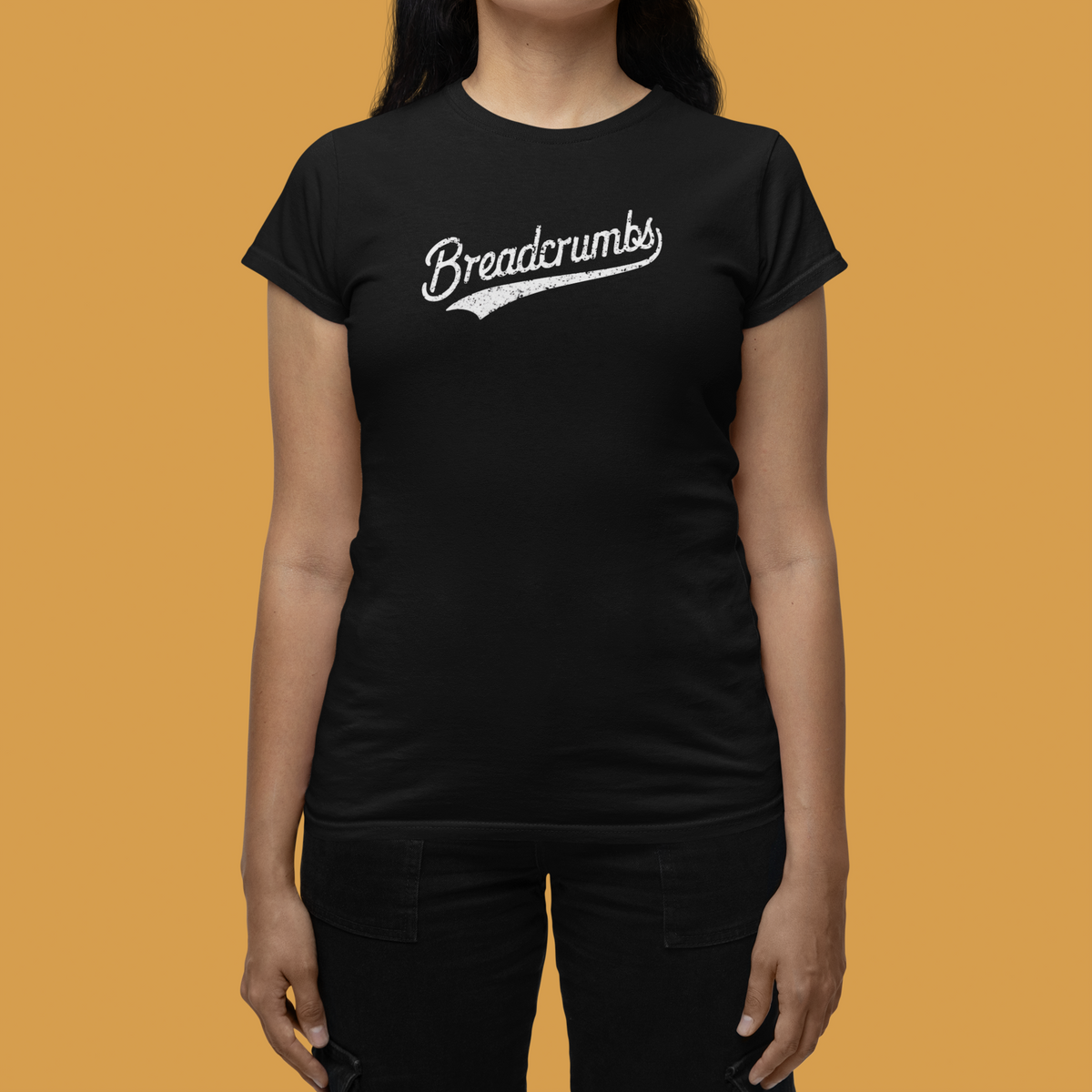 'Breadcrumbs' t-shirt in black, woman wearing it against a yellow backdrop, funny retro script logo tee gift