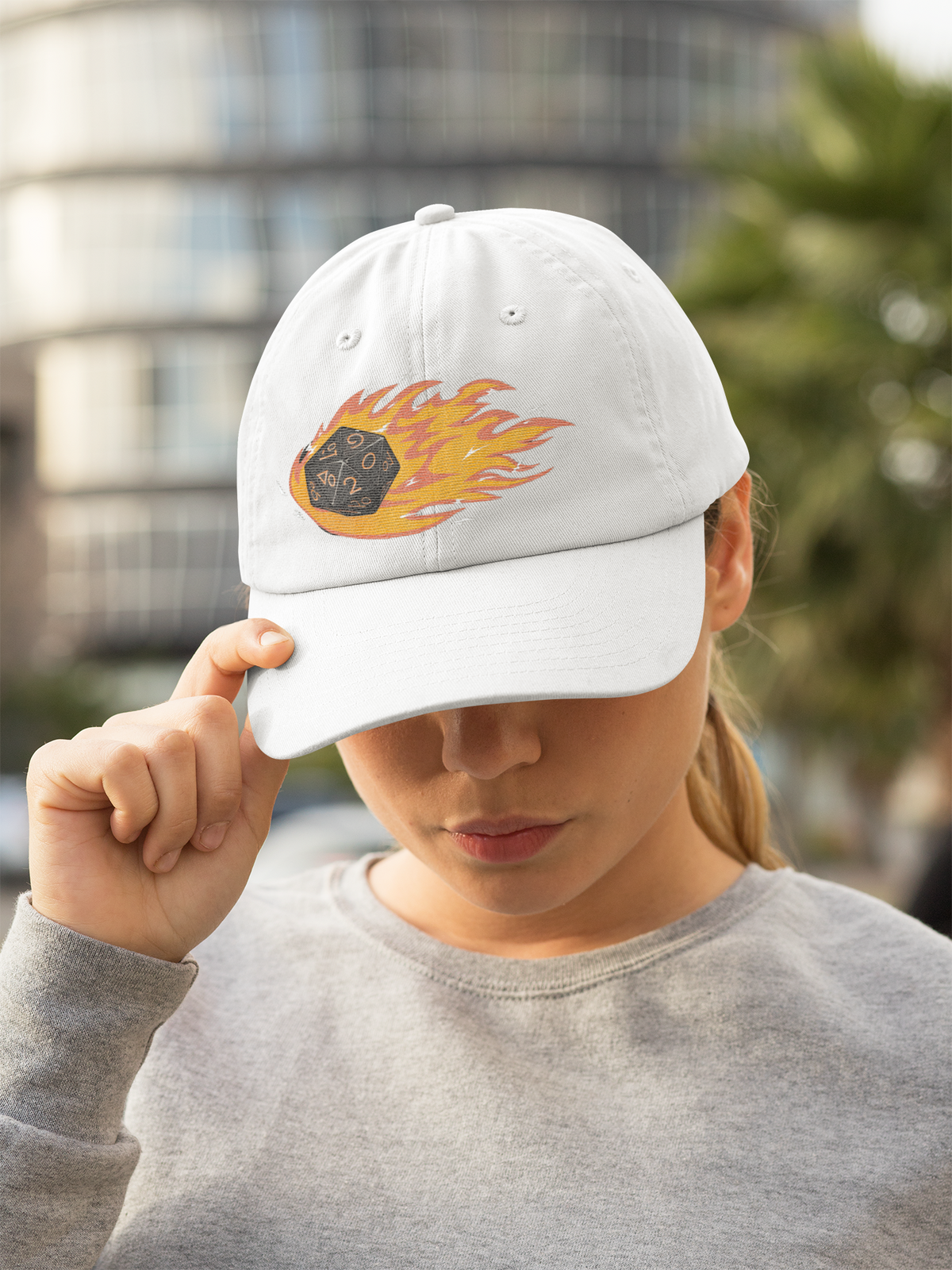"Polyhedral Dice On Fire" dad hat in white, woman wearing it outdoors in the city, funny gamer gift