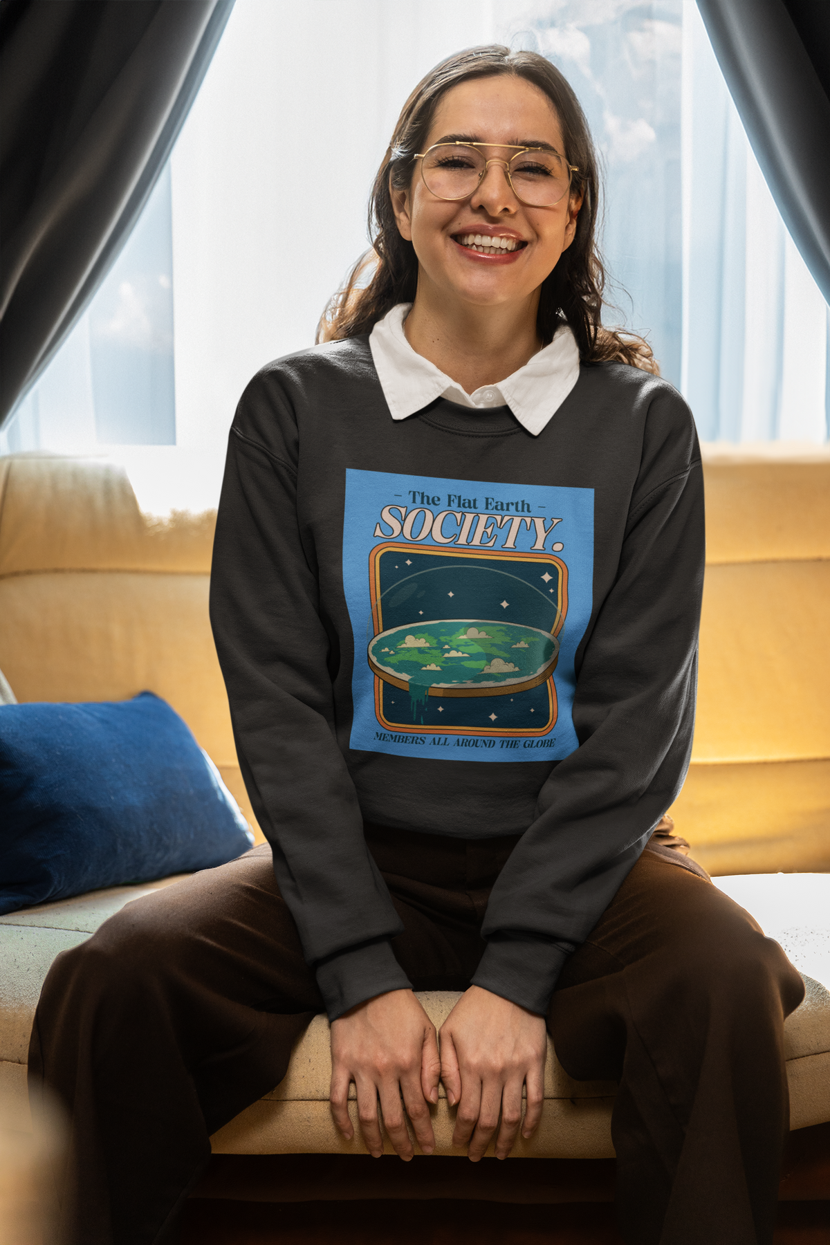 'The Flat Earth Society' sweatshirt in charcoal, woman wearing it seated, funny satire gift idea