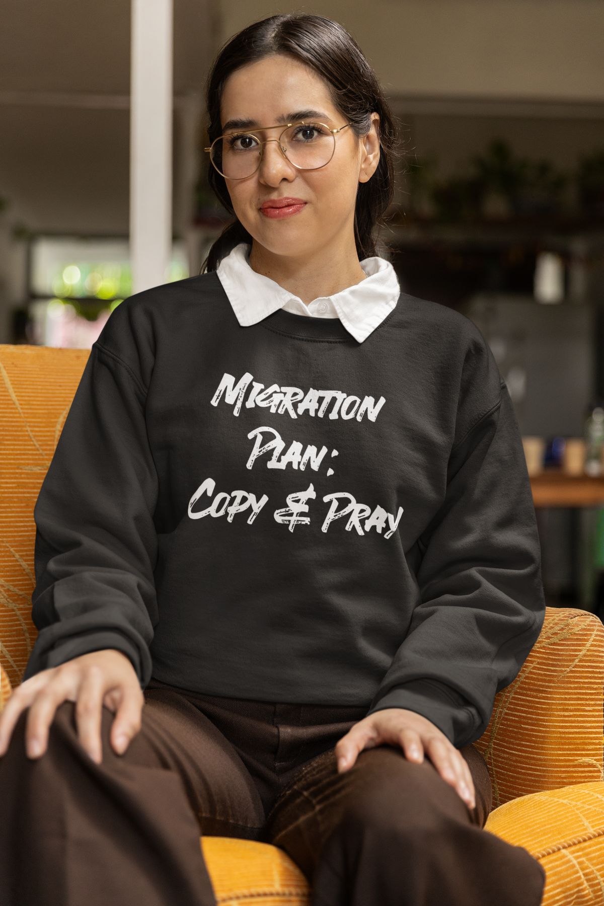 'Migration Plan: Copy and Pray' sweatshirt in black, woman with glasses sitting indoors, funny developer gift