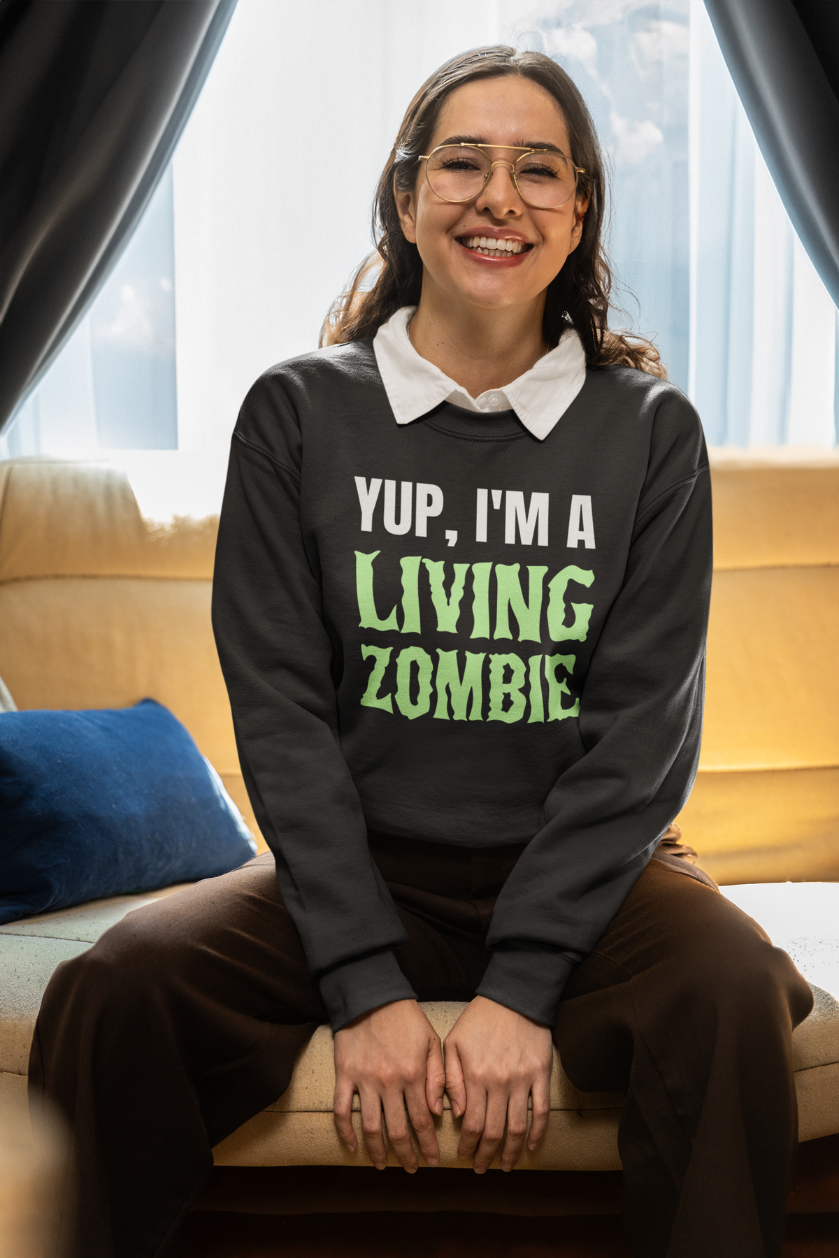 'Yup, I'm a Living Zombie' sweatshirt in black, woman wearing it seated indoors, funny horror gift